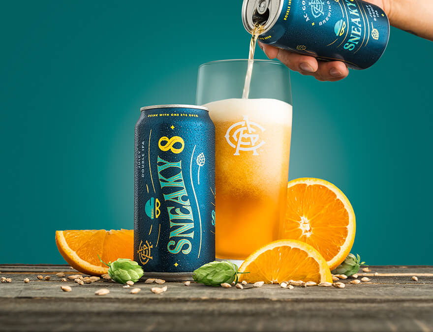 Sneaky 8 can, and hand pouring juice over glass on a table with orange chunks